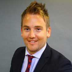 Andrea-Smith Man smiling wearing a black suit and tie